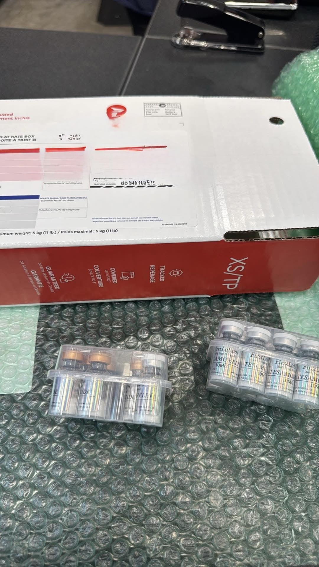 Canada Post XS flat rate box next to FirstLabs PH Tesamorelin 10mg vials in protective packaging